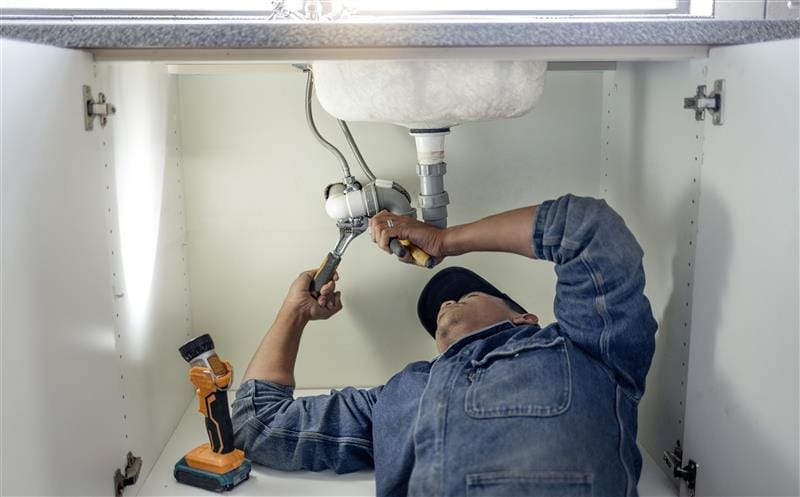 Plumber repairing pipes beneath a bathroom sink in Thousand Oaks